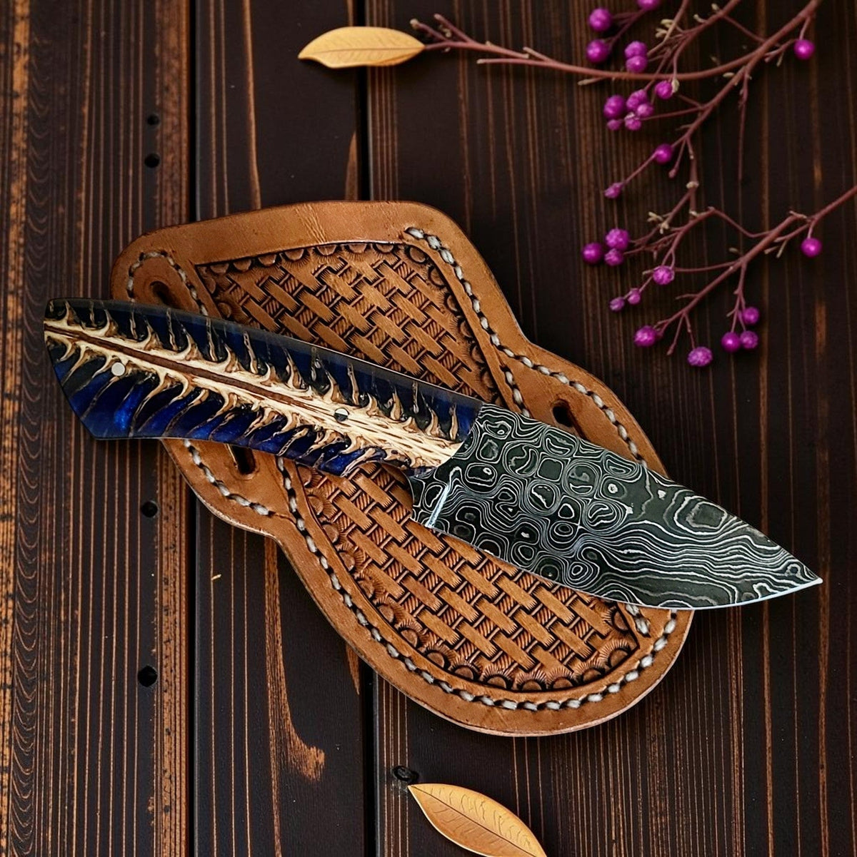 The Blue Norther knife with a Damascus blade and blue resin handle on its tooled leather sheath