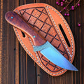 Working Cowboy Knives with wooden handle and blue blade in a brown leather sheath on a wooden surface.