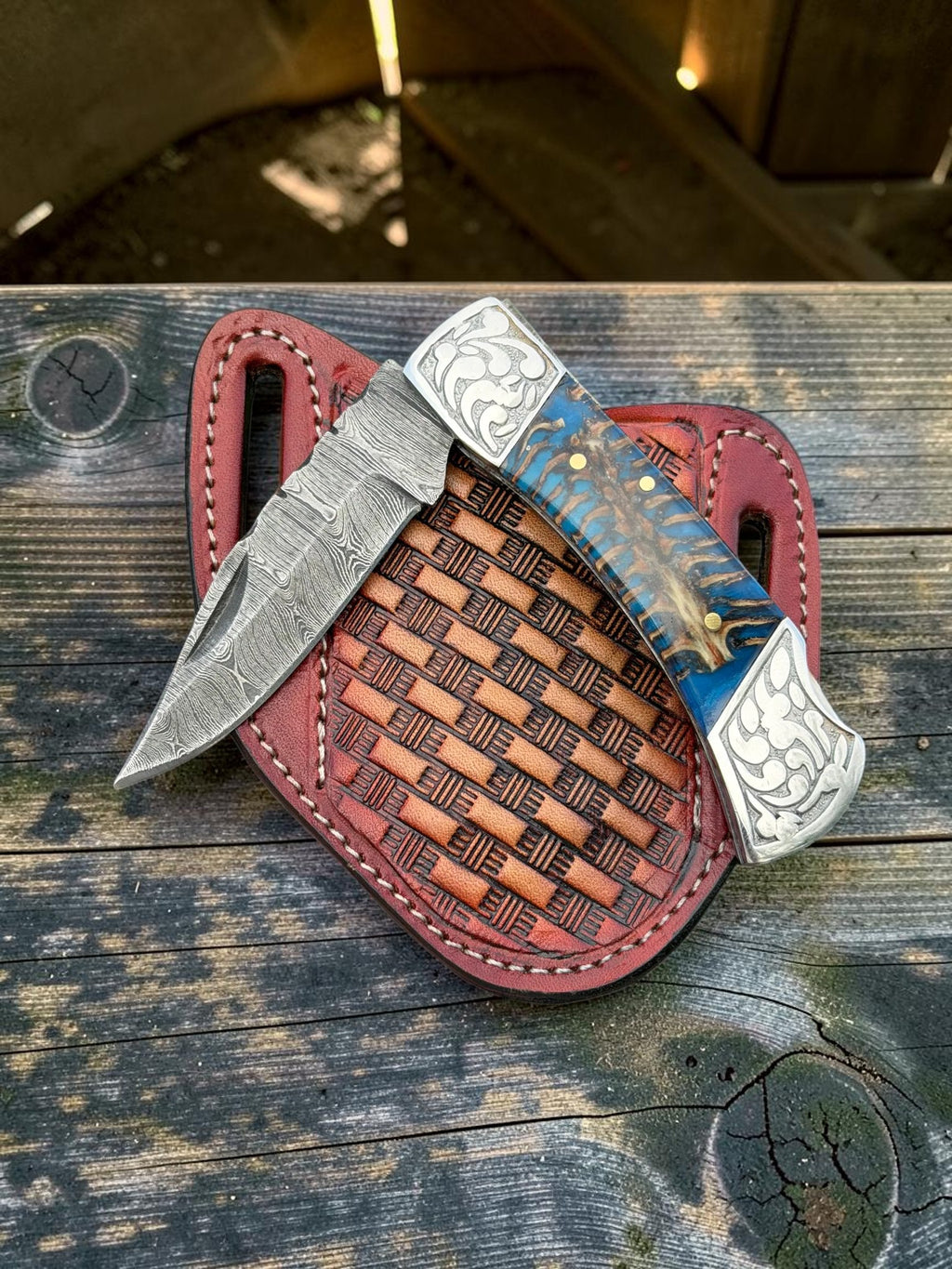 Handmade Damascus Pocket Knife with a 3-inch Damascus steel blade, Blue Epoxy Pine Cone Resin handle, engraved steel bolster, back lock mechanism, and leather cross draw sheath.