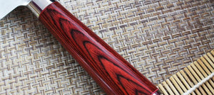 A close-up of a kitchen knife with a glossy dark reddish-brown wooden handle and a silver metal blade, resting on a woven straw mat.